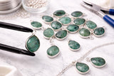 Close up of natural emerald gemstone charm showing deep green stone set in sterling silver bezel jewelry charm