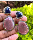 Blue and salmon sapphire diamond earrings held in manicured hand, natural gemstone detail with sterling silver setting