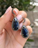 Natural blue sapphire diamond drop earrings in sterling silver displayed between fingers .