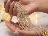 Thirteen-inch strand of small faceted Golden Rutilated Quartz beads with clear and pale golden tones shown on womans hand