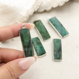 Emerald gemstone charm held between fingers to show its size and elongated rectangular shape