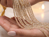 Detailed macro view of rutilated quartz beads with varied golden rutile patterns and natural inclusions shown on womans hand