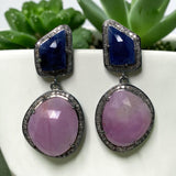 Untreated pink and blue sapphire earrings with genuine pave diamonds photographed upright against green plants