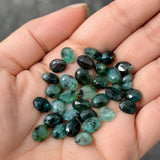 Natural emerald rose cut cabochons held in hand showing freeform shapes, size and green color variations
