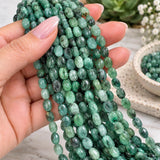 Natural Emerald smooth oval bead strands held in hand showing bead scale, polished finish and natural green color variations