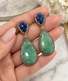 Natural emerald and blue sapphire pave diamond long drop earrings shown in hand with green and deep blue gemstones