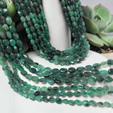 Natural Emerald smooth oval gemstone bead strands displayed around a white succulent  pot showing rich green tones and polished beads for jewelry making.