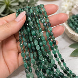 Natural Emerald smooth oval gemstone bead strands held in hand, showing green color variations, polished finish and bead size for jewelry making.