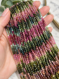 Natural Tourmaline round bead strands held in hand showing bead scale and natural pink green multicolor variations