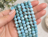 AAA natural Dominican Larimar beads held in hand showing bead size, ocean blue color, white patterns and smooth polished finish