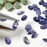 Natural iolite faceted gemstones displayed with jewelry tweezers on a white background