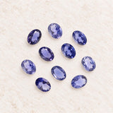 Natural iolite oval gemstones arranged together on a soft ivory surface, approximately 5x3.75mm each